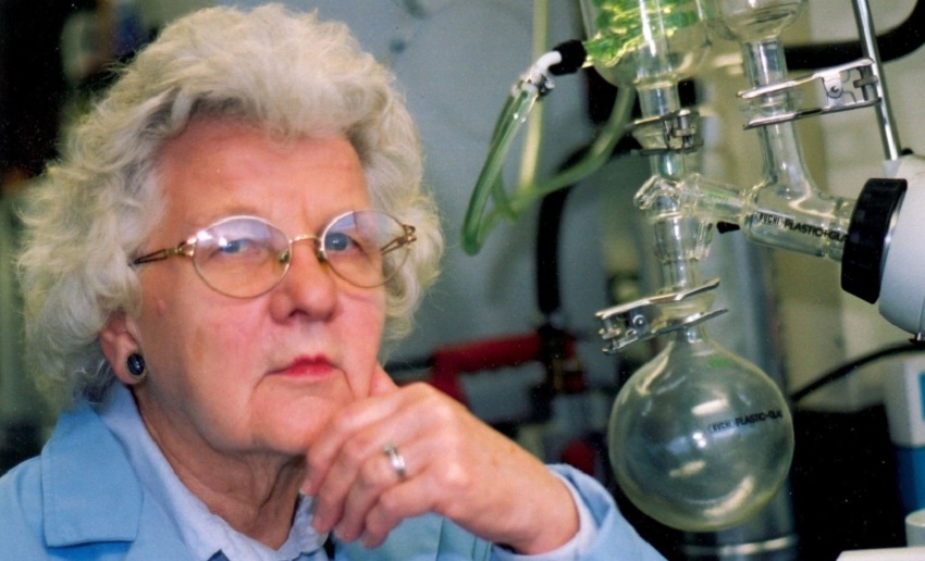 a woman with white hair sitting next to a chemistry apparatus