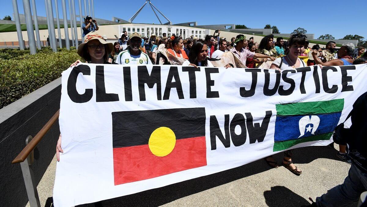 Aboriginal and Torres Strait Islander people, alongside non-Indigenous allies, holding a banner that says Climate justice now
