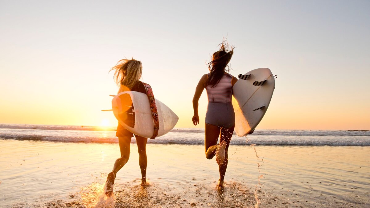 Tw young women running into the ocean with surfboards under their arms