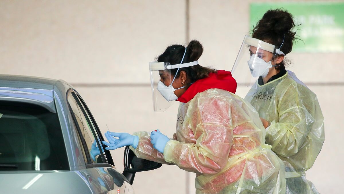 Two nurses in biosecurity clothing looking into a car window
