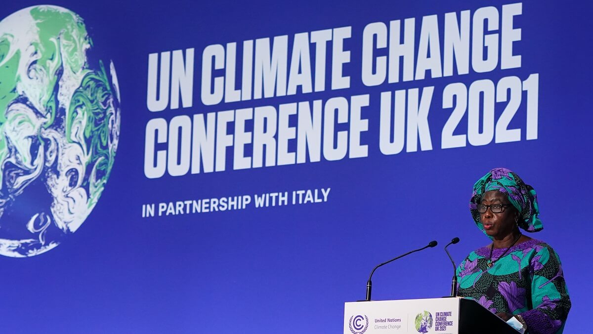 A woman standing in front of a screen with words that say "UN climate change conference UK 2021"