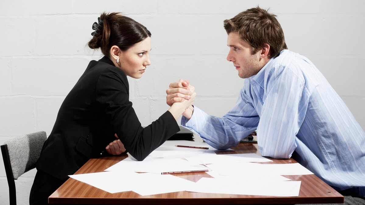 Woman and man in business attire, arm wrestling on a table
