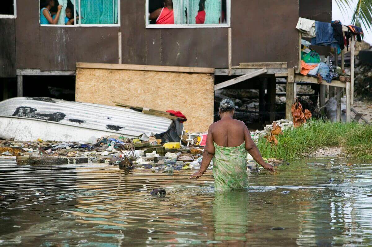 A woman wades through floodwaters among a wrecked house