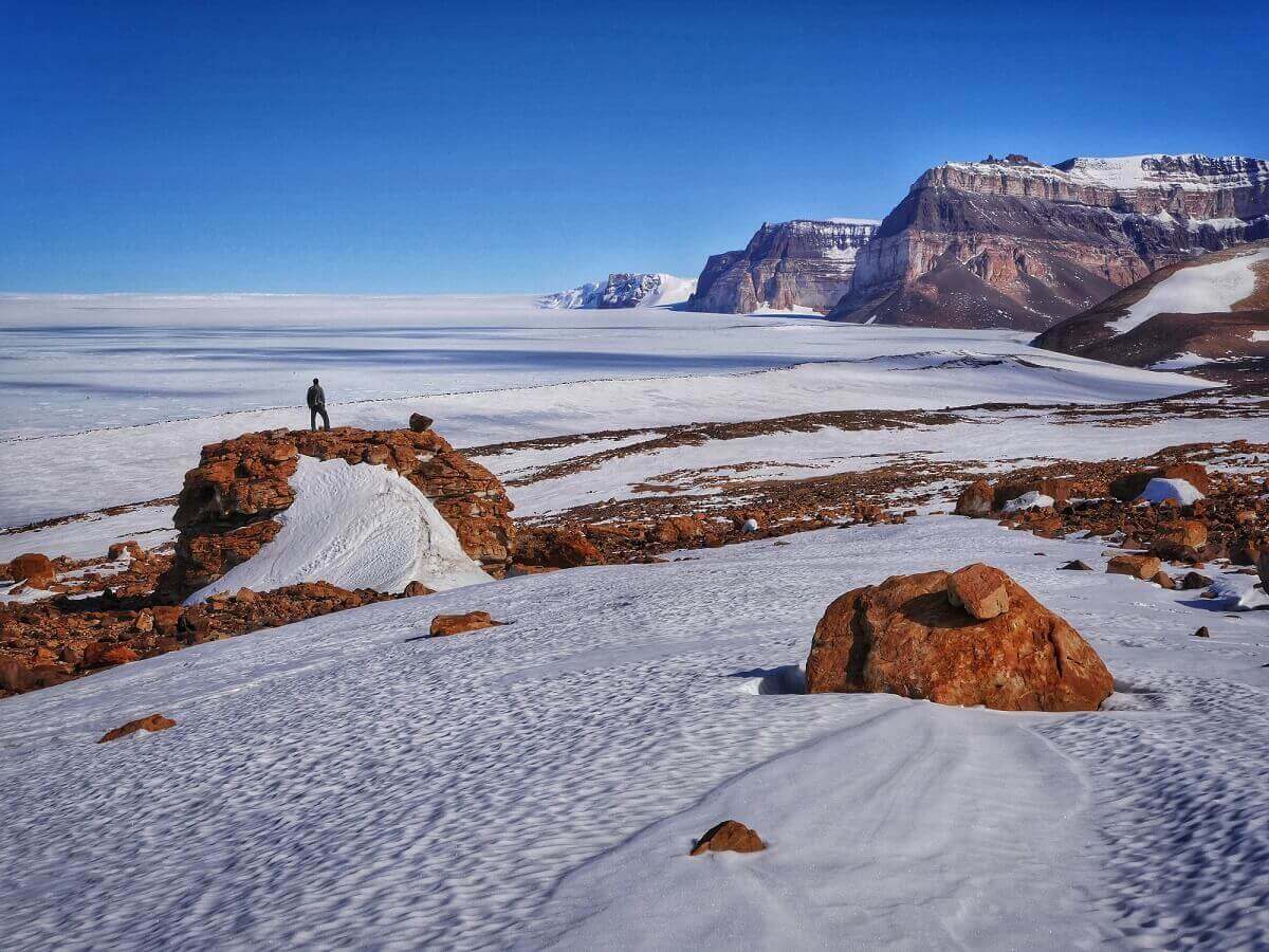 Man standing on red rock in rocky and icy landscape