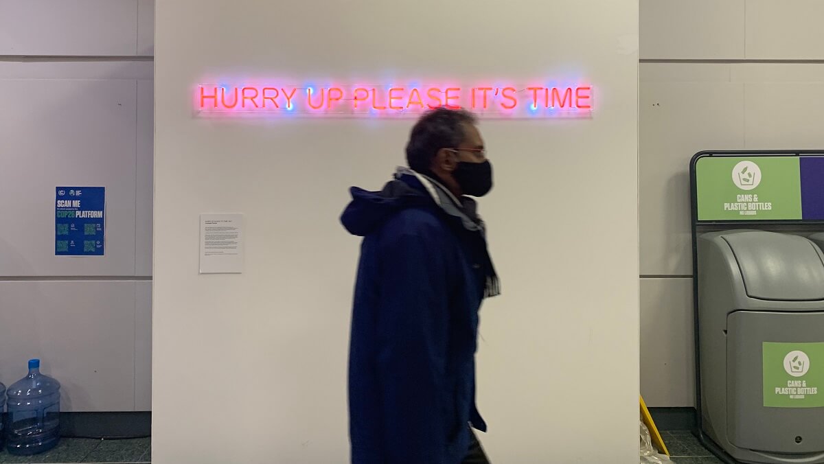 Man walking past sign that says "hurry up please it's time"