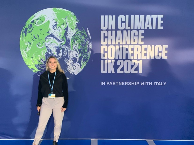 Young woman stands in front of cop26 sign