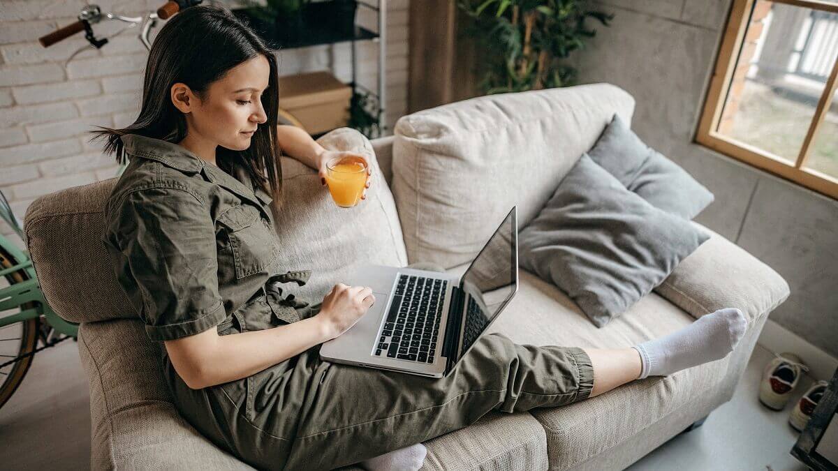 Woman sitting on a couch with a cup of tea and a laptop