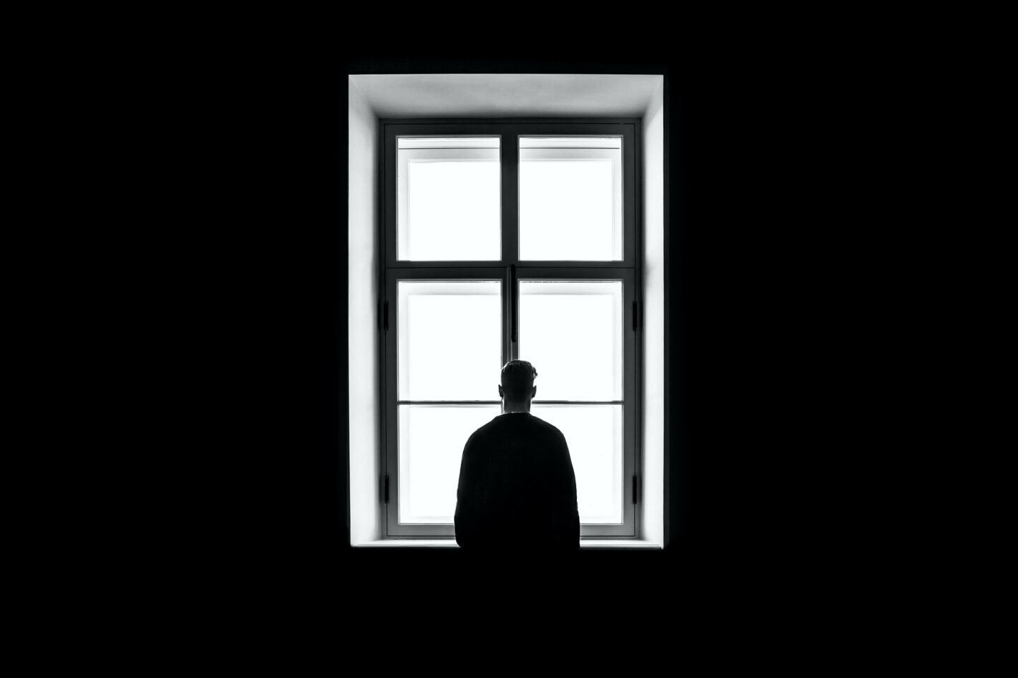Silhouette of man looking out of window