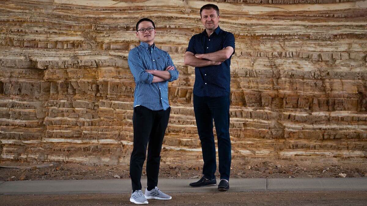 Professor Hrvoje Tkalčić and Sheng Wang standing in front of a rock wall layered like a cake