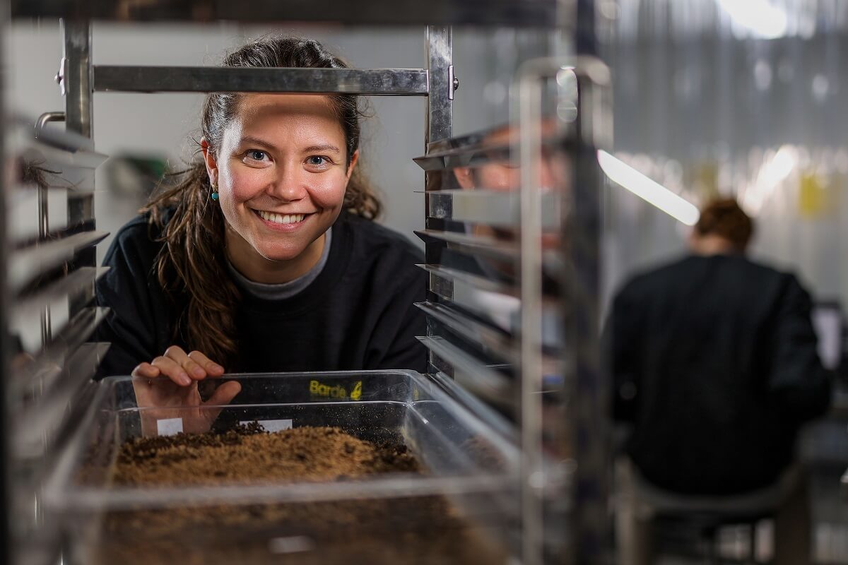 Young woman smiling at camera through rack of trays with soil