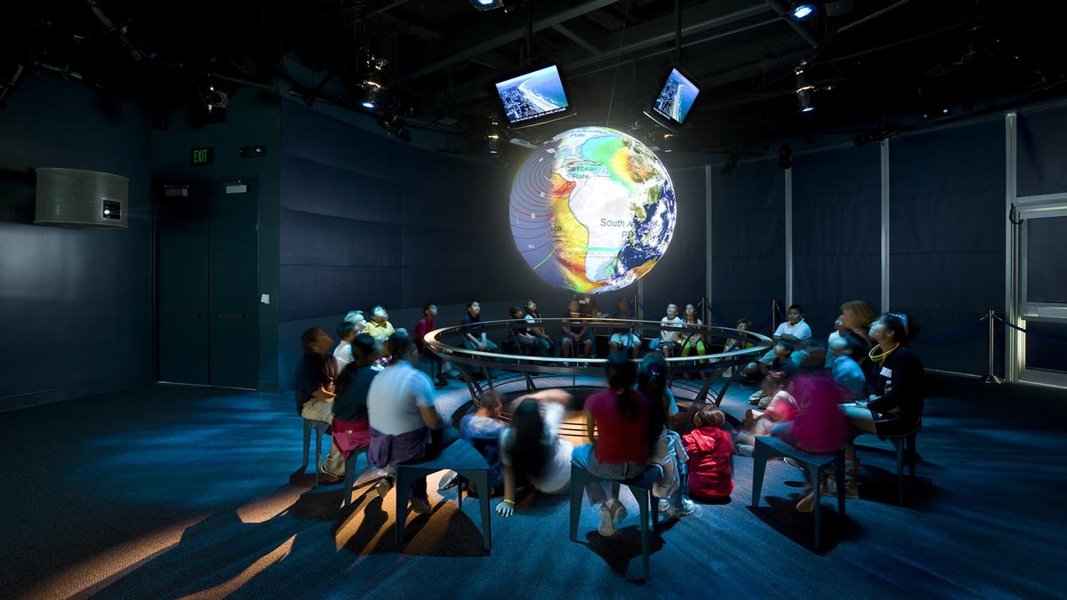 people in a museum looking at an illuminated digital globe