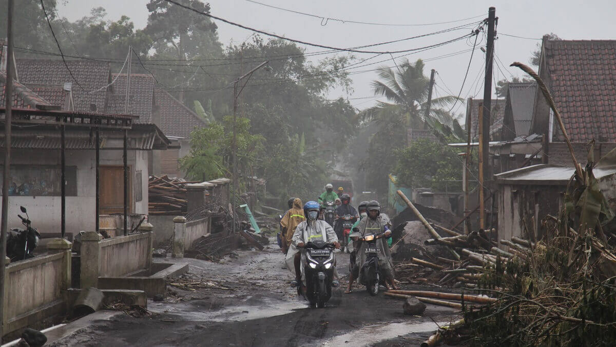 People rise motorcycles through a village filled with thick mud and debris.