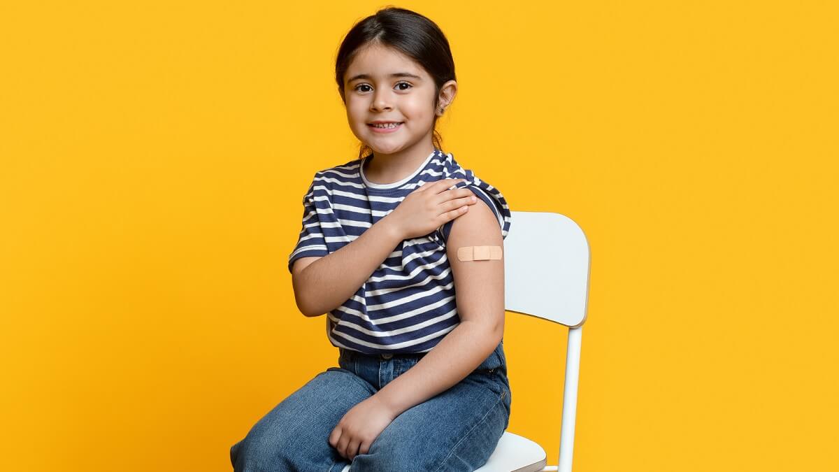 Little girl sits on chair showing bandaid on left arm