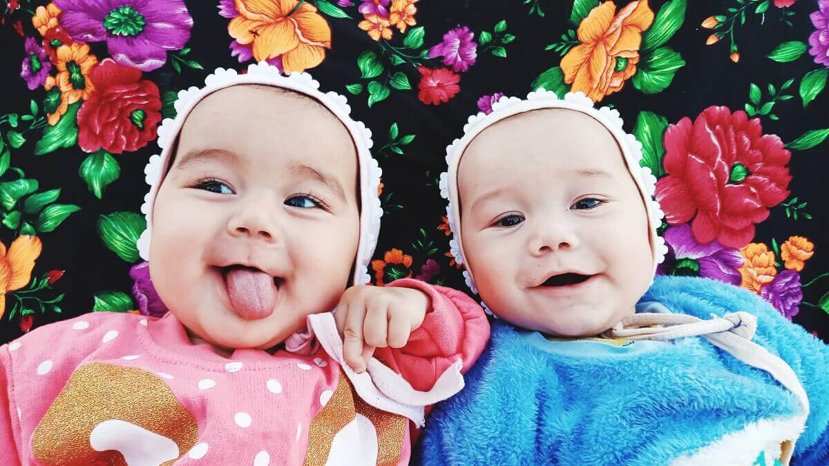 Two smiling babies, one is dressed in pink, the other is dressed in blue.