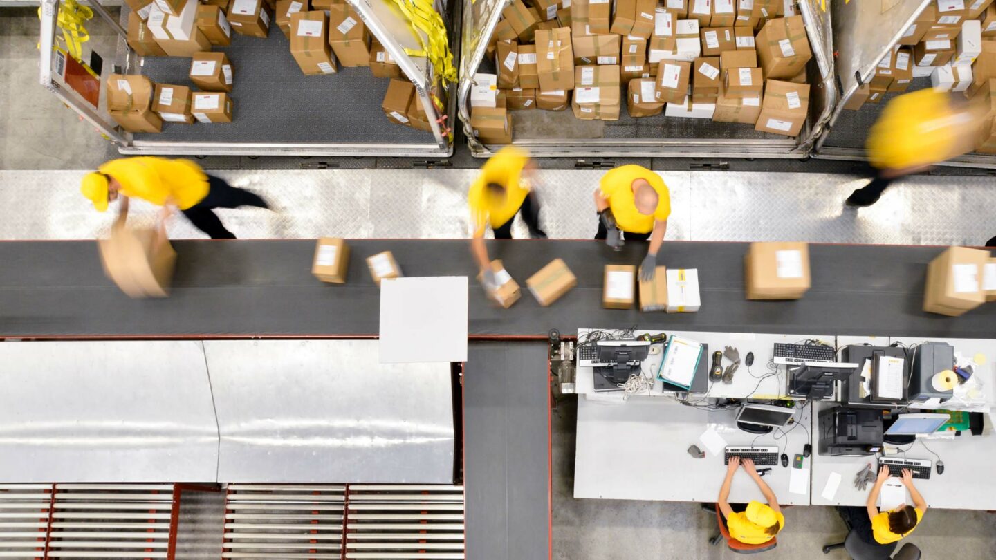 aerial photo of people in warehouse sorting packages on a conveyor belt