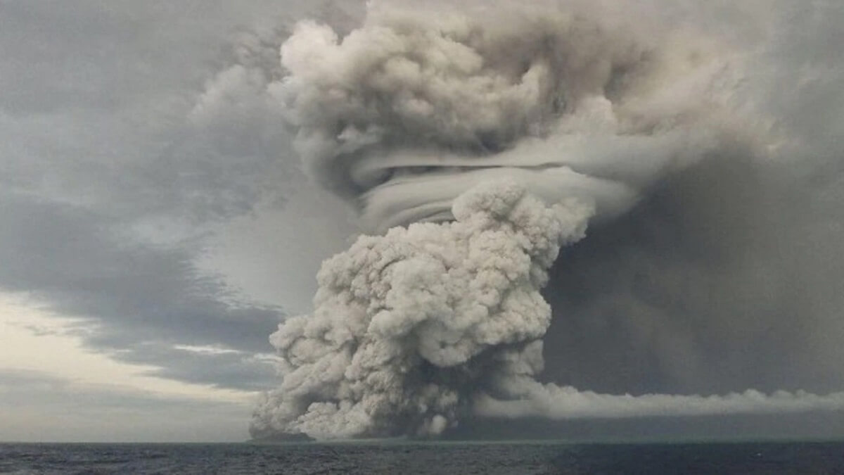 An ash cloud reaches into the sky above an actively erupting oceanic volcano.