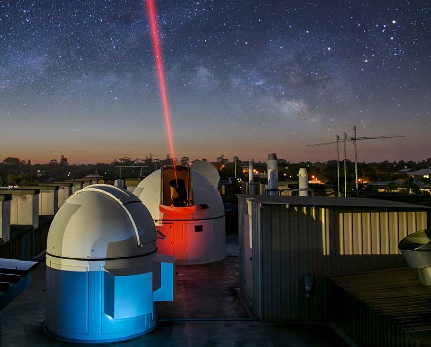 Large machine shooting a red laser into the night sky with stars in the background