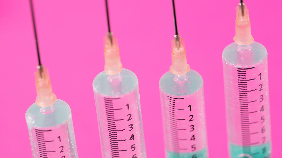 Four syringes against a pink background