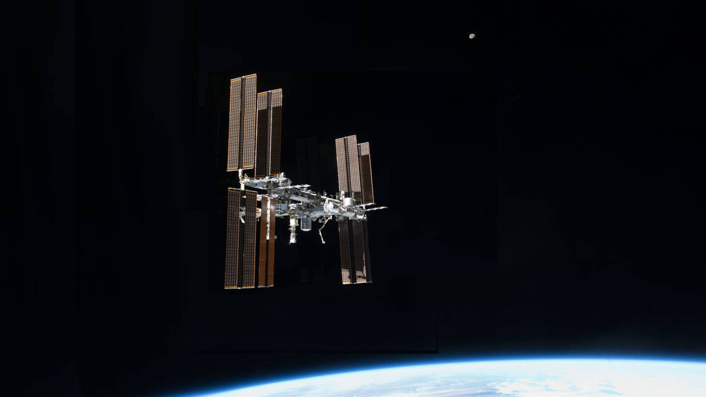international space station in space above earth with small moon in the distance