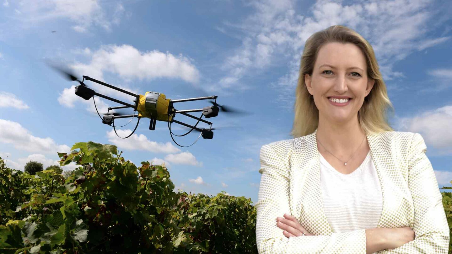 catherine ball smiling and standing in front of a drone flying through a vineyard