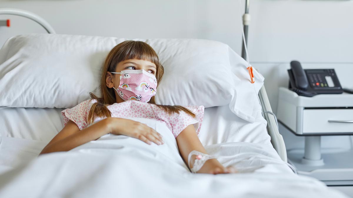 omicron in kids concept young girl lying in hospital bed wearing a face mask