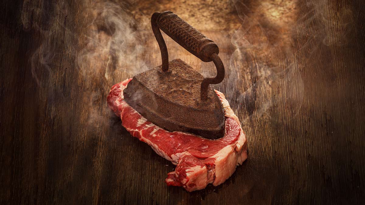 how to cook the perfect steak concept a rib eye steak being pressed with a hot old-fashioned iron