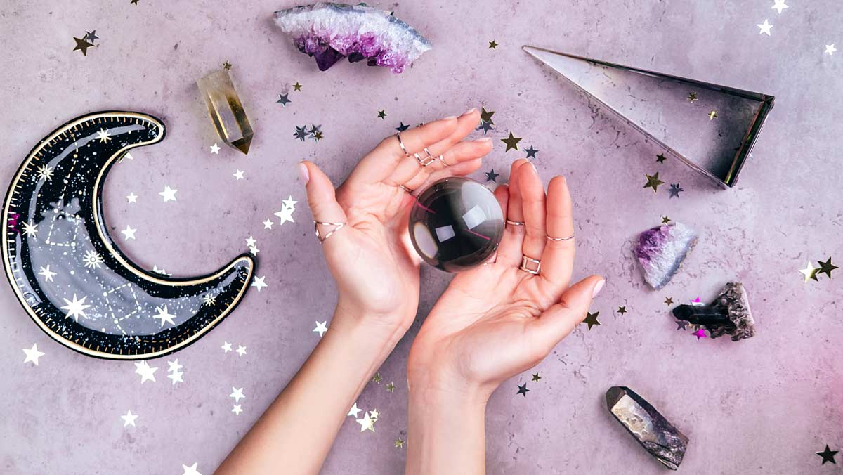 hands holding a crystal ball over a flat lay of various crystals and sequins