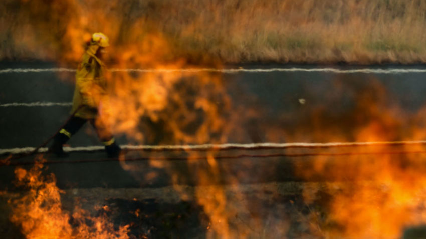 Firefighter health concept firefighter walking on a road behind flames from a bushfire