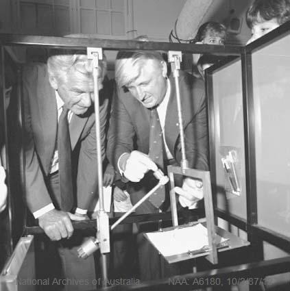 Black and white photo of mike gore and bob hawke examining pendulum