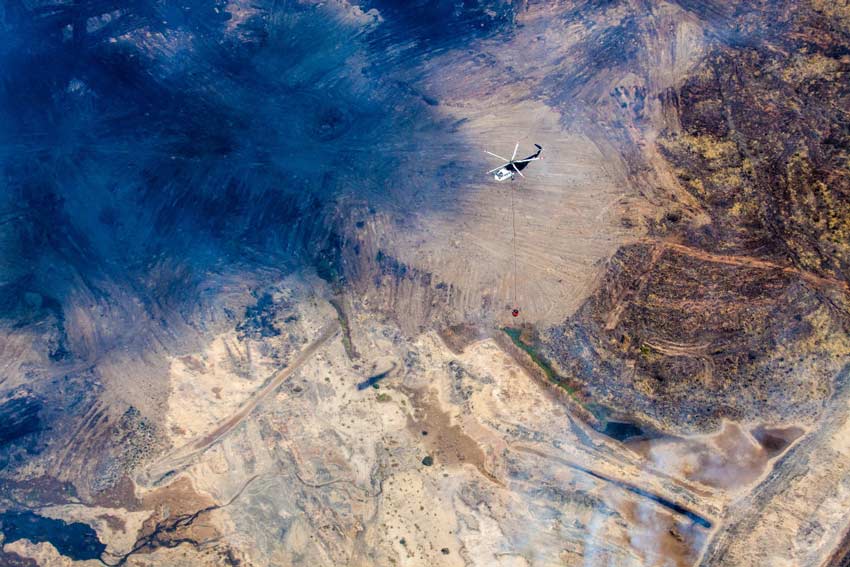 Aerial view of a barren and burnt landscape with a helicopter flying above