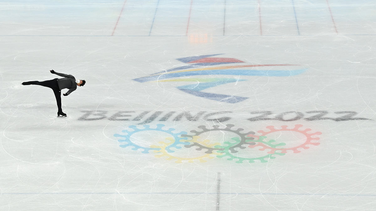 covid olympics concept an olympic ice skater on a rink wearing a face mask with the words beijing 2022 and the olympic rings shaped like coronavirus on the ice