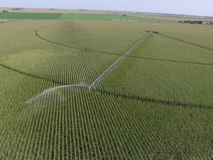 An aerial view of a corn field being watered by center pivot irrigation.