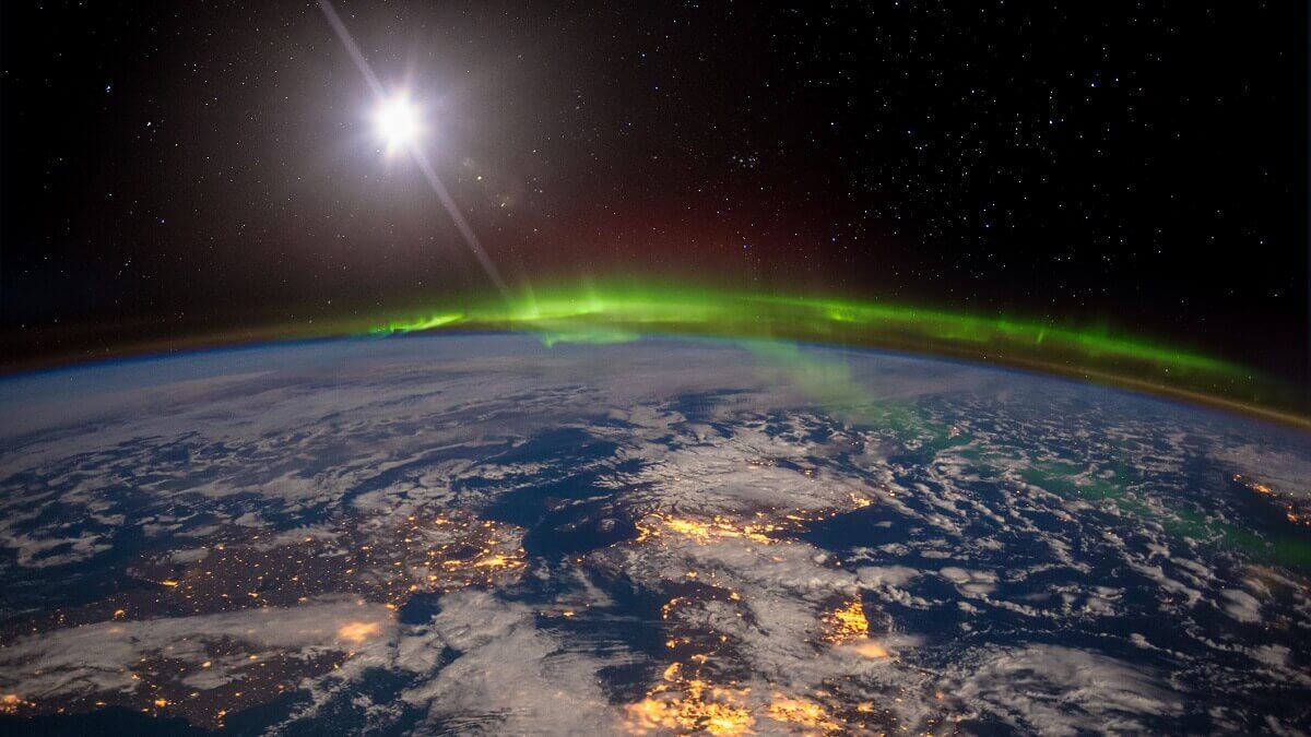 Earth from space under an aurora with the sun behind it.