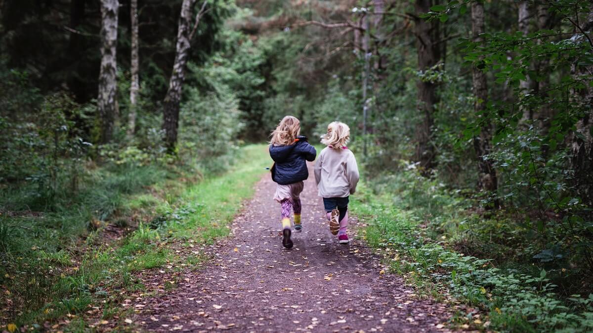 Two children run side by side along forest path