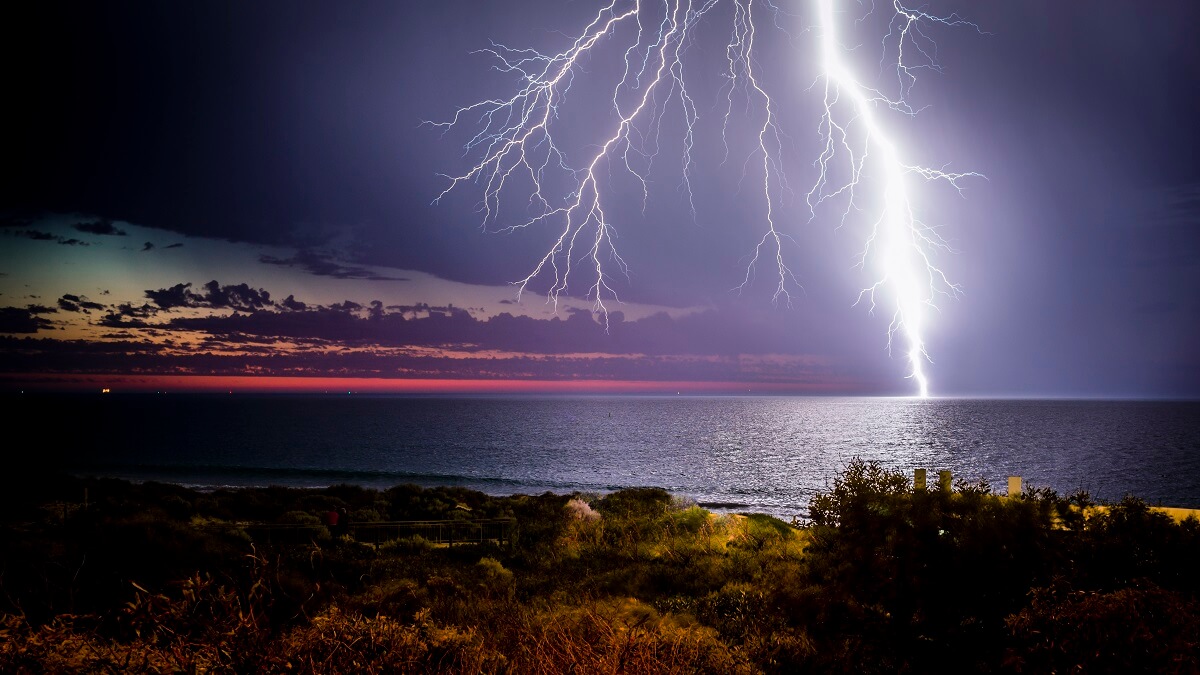 Lightning flashes over the ocean at sunset.