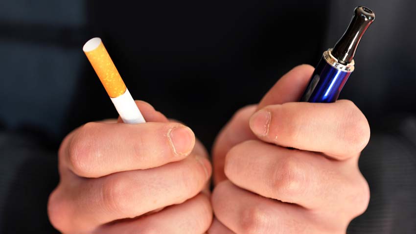 E-cigarette use and gum disease concept a person holding an e-cigarette in one hand and a conventional cigarette in the other