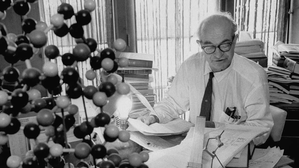 black and white photograph of linus pauling seated at his desk with papers and chemical models