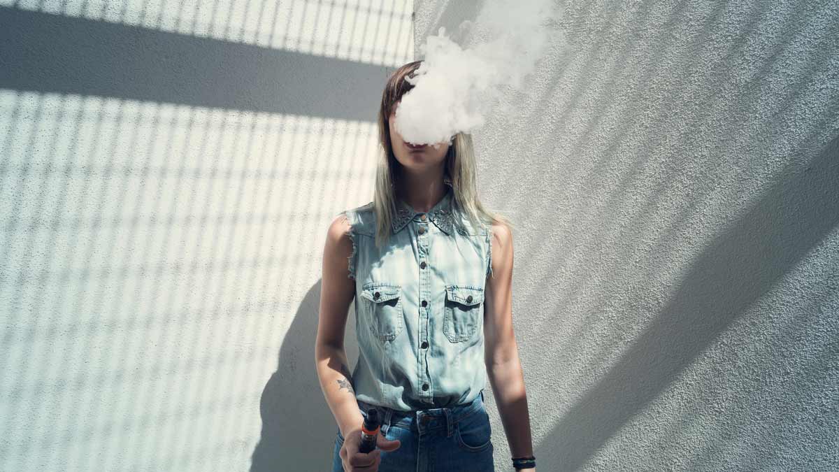 e-cigarette use and gum disease concept a young woman smoking an e-cigarette with a cloud of vapour covering her face