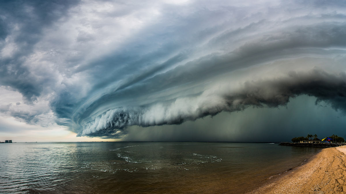 wide angle photograph of huge storm cloud forming over the ocean and a little bit of the beach