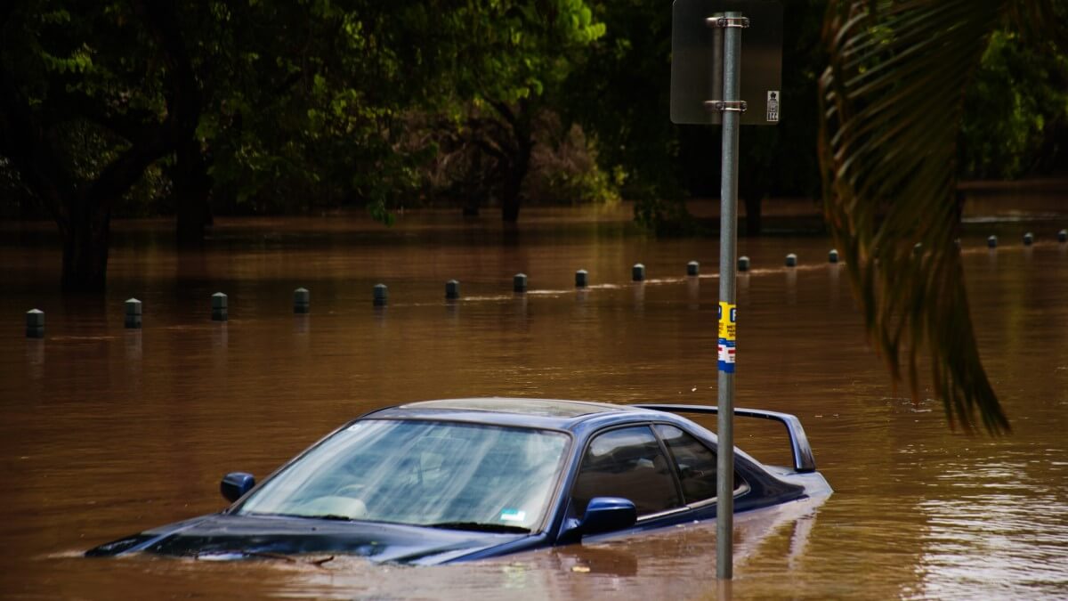 car half submerged in brown floodwater next to a sign