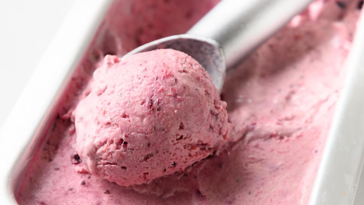 Berry ice cream being scooped out of a tub