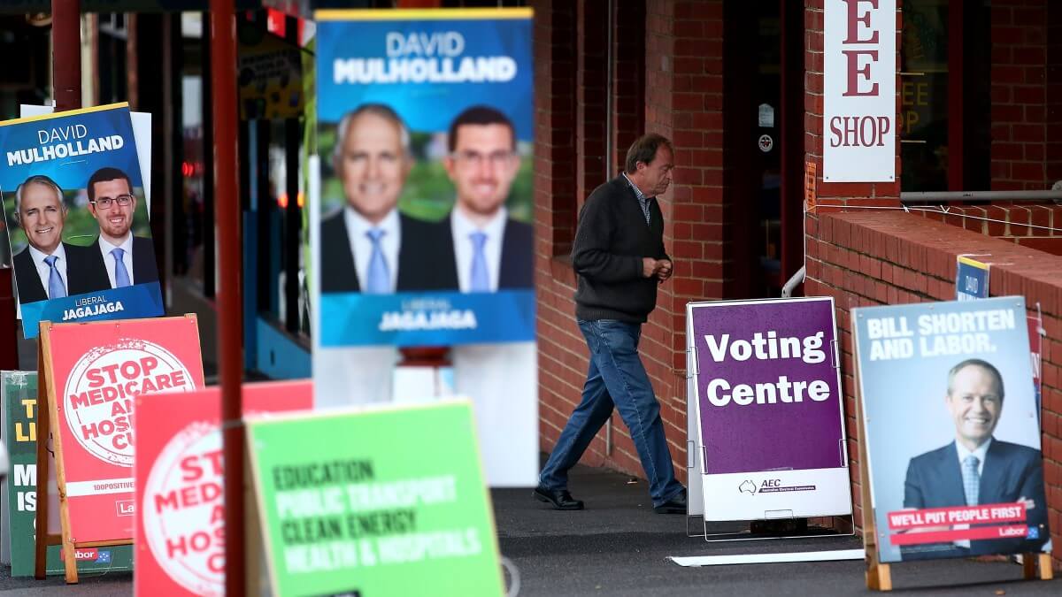 person walking into a building marked with sign sayinf 'Voting Centre', surrounded by corflute signs