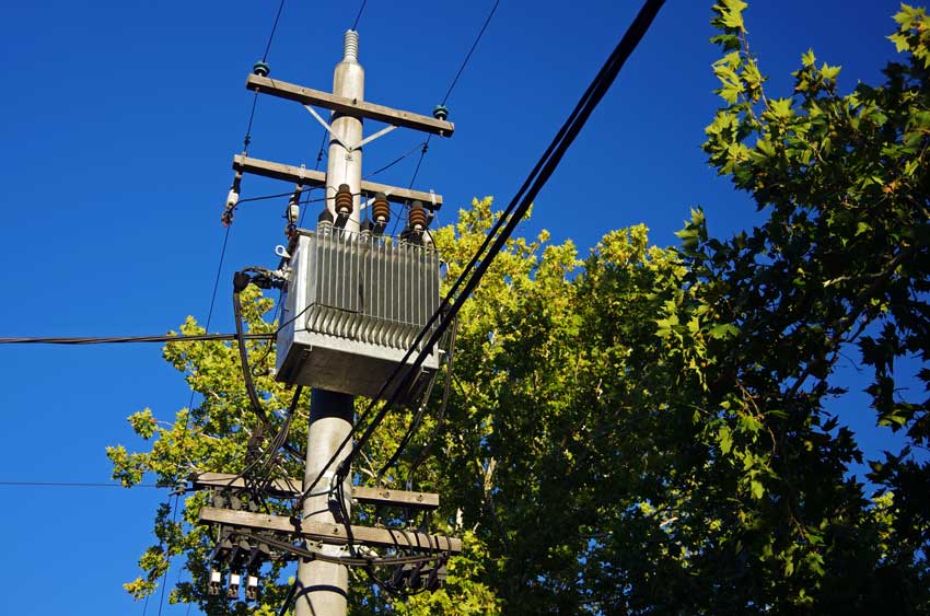 What is the grid concept photo of a transformer on a concrete pole and some power lines against leaves and a blue sky in the background