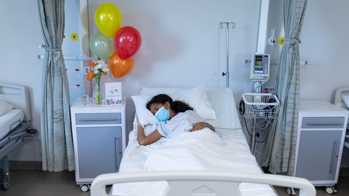 girl lying in hospital bed with ballons and flowers