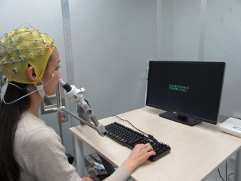 Person wearing a skullcap covered in wires sits in front of a computer, with a tube-like device positioned up their nose