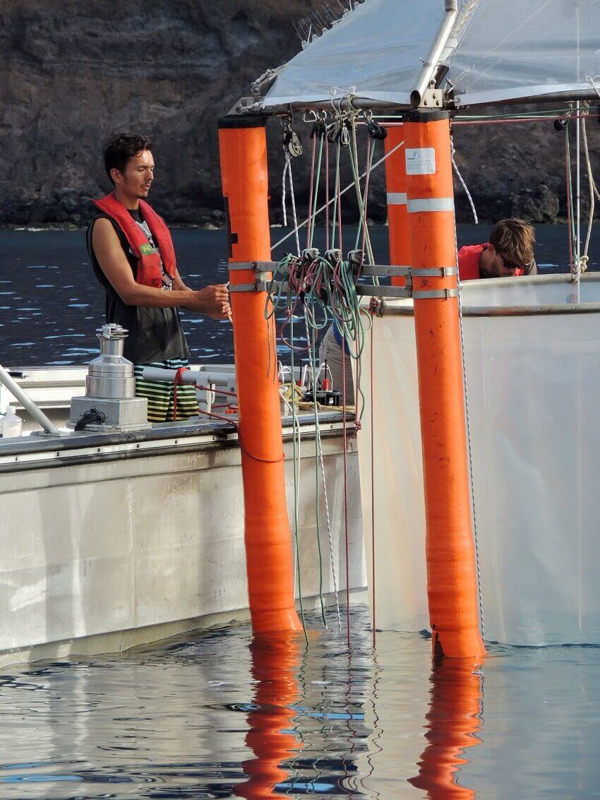 Person on a boat lowering cylindrical net several metres in diametre connected to floats into the ocean