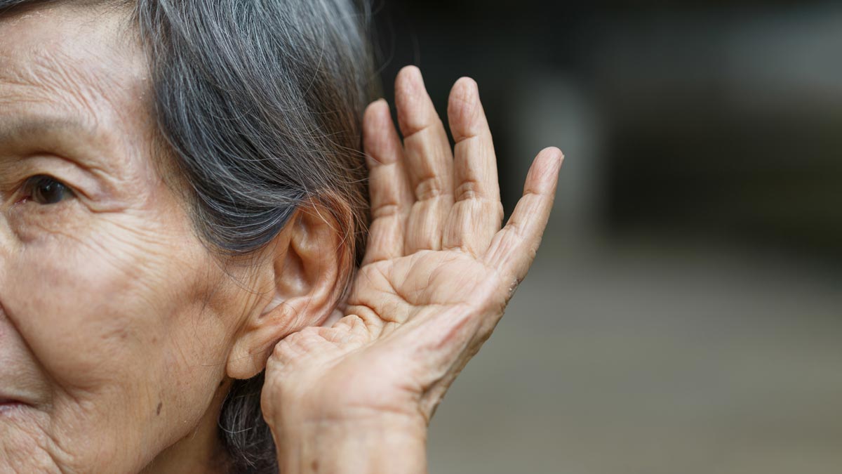 reverse hearing loss concept closeup photograph of an elderly woman holding a hand to her ear
