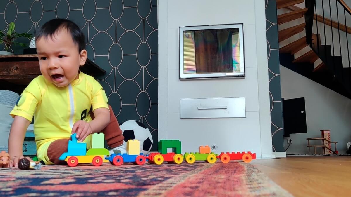 baby inside a home playing with a toy train and wearing a smart jumpsuit, a yellow jumpsuit with round sensors visible in sleeves
