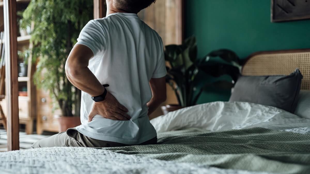 A man suffering from low back pain sitting on a bed.