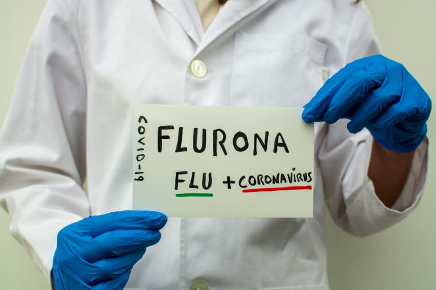 Flurona concept a person in ppe holding a hand-written sign that says flurona flu plus coronavirus